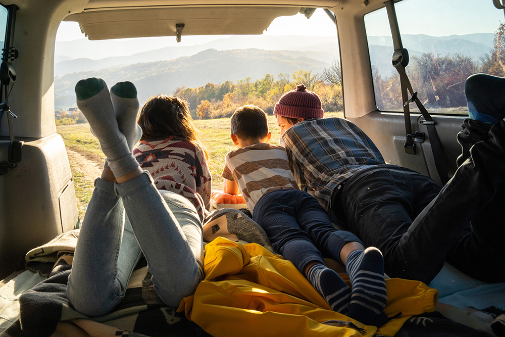 A family,  in the back of a car, looking into the mountain vista. 