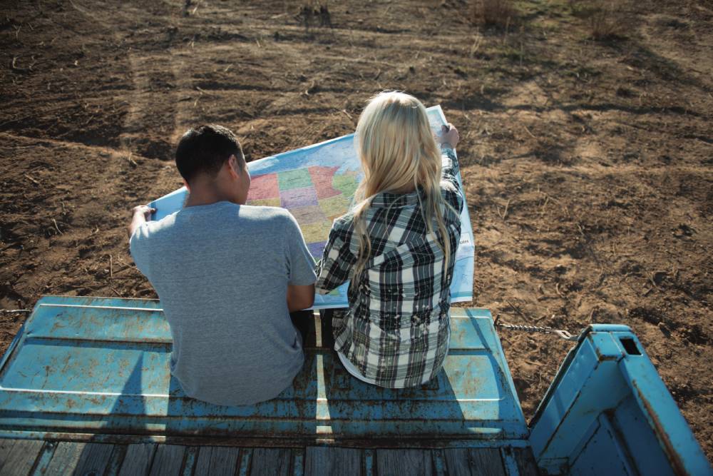 On-page, 2024. Two friends sitting on a truck bed and holding a U.S. map.