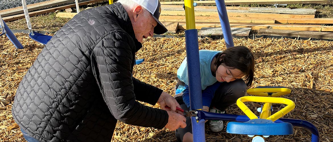 Mountain Shadow Association elder helps child fix playground equipment